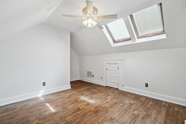 additional living space with vaulted ceiling with skylight, dark hardwood / wood-style floors, and ceiling fan