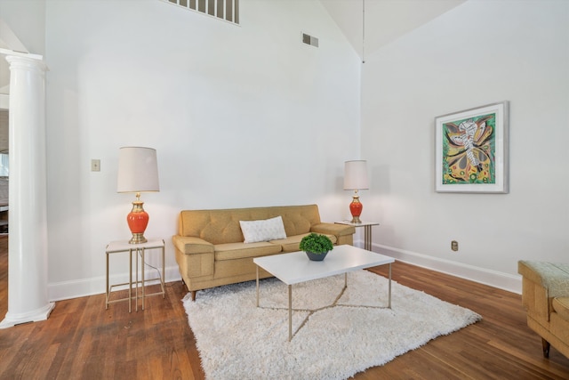 living room featuring dark wood-type flooring, decorative columns, and high vaulted ceiling