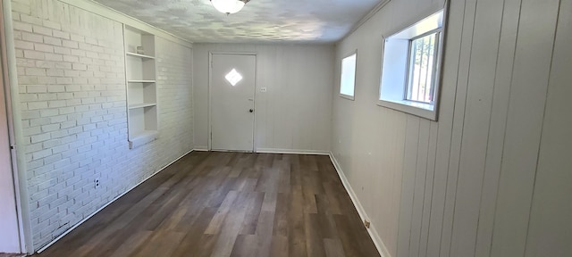 doorway to outside featuring brick wall, dark hardwood / wood-style flooring, a textured ceiling, crown molding, and built in features