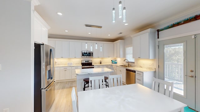 kitchen featuring appliances with stainless steel finishes, hanging light fixtures, white cabinets, a center island, and sink