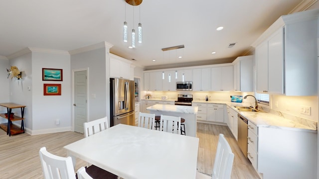 kitchen with light wood-type flooring, white cabinetry, a kitchen island, stainless steel appliances, and decorative light fixtures