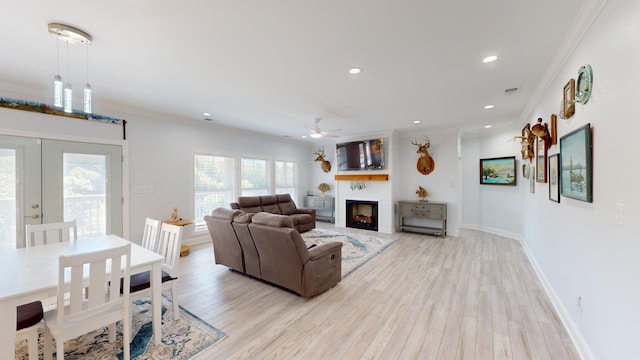 living room featuring light hardwood / wood-style flooring, a large fireplace, ceiling fan, and ornamental molding