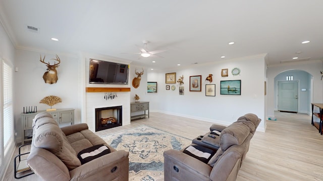 living room with ornamental molding, a large fireplace, light hardwood / wood-style floors, and ceiling fan