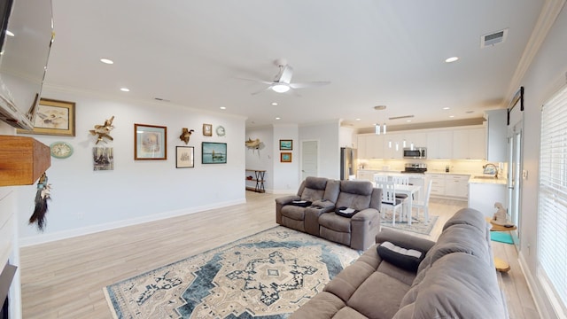 living room featuring light wood-type flooring, ornamental molding, sink, and ceiling fan