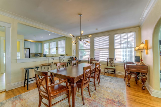 dining area featuring light wood-type flooring, a healthy amount of sunlight, crown molding, and a notable chandelier