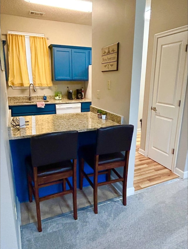 kitchen featuring a breakfast bar, white dishwasher, kitchen peninsula, hardwood / wood-style floors, and blue cabinets