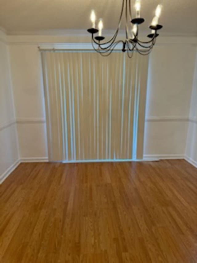 unfurnished dining area featuring wood-type flooring, a notable chandelier, and ornamental molding