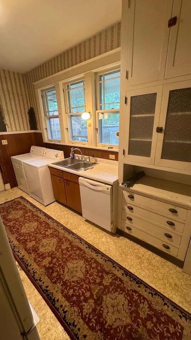 kitchen featuring washing machine and clothes dryer, a wealth of natural light, sink, and white dishwasher