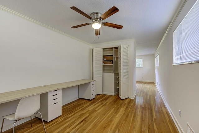 unfurnished office featuring light hardwood / wood-style flooring, built in desk, ceiling fan, and crown molding