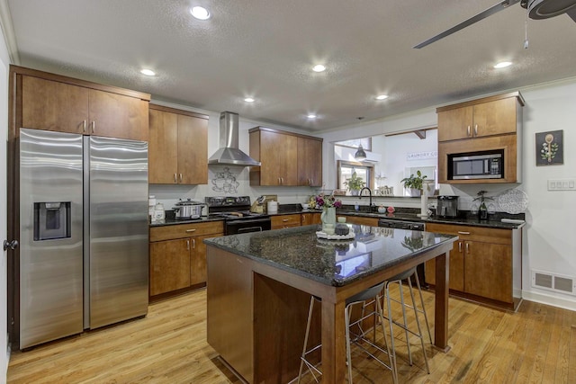 kitchen with light hardwood / wood-style floors, a kitchen island, wall chimney range hood, black / electric stove, and stainless steel fridge