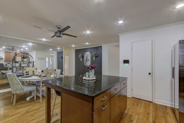 kitchen with light wood-type flooring, a textured ceiling, a center island, ceiling fan, and ornamental molding