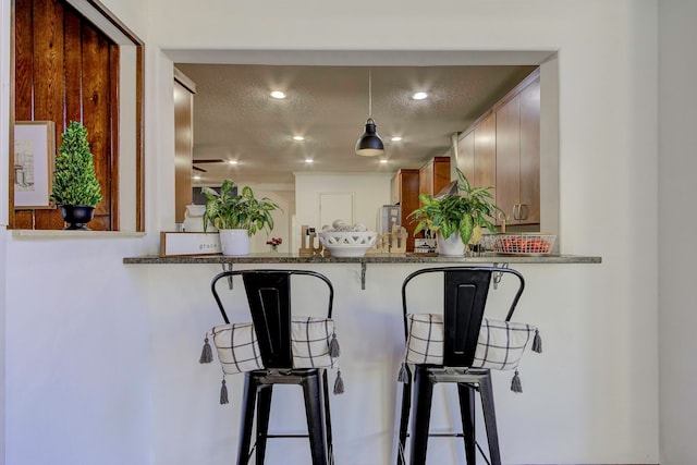 kitchen with decorative light fixtures, a textured ceiling, a kitchen breakfast bar, and stone counters