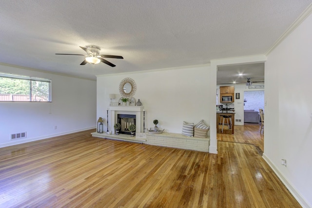 unfurnished living room with ceiling fan, a textured ceiling, ornamental molding, and wood-type flooring