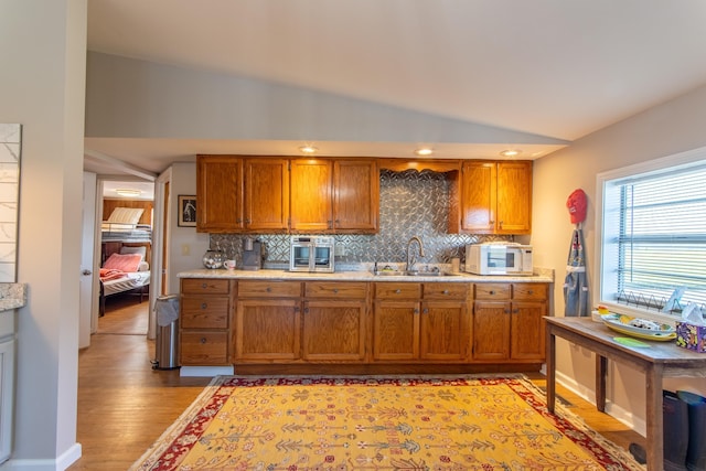 kitchen with lofted ceiling, brown cabinetry, a sink, and white microwave
