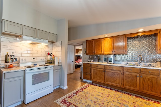 kitchen with backsplash, white electric range, under cabinet range hood, and a sink