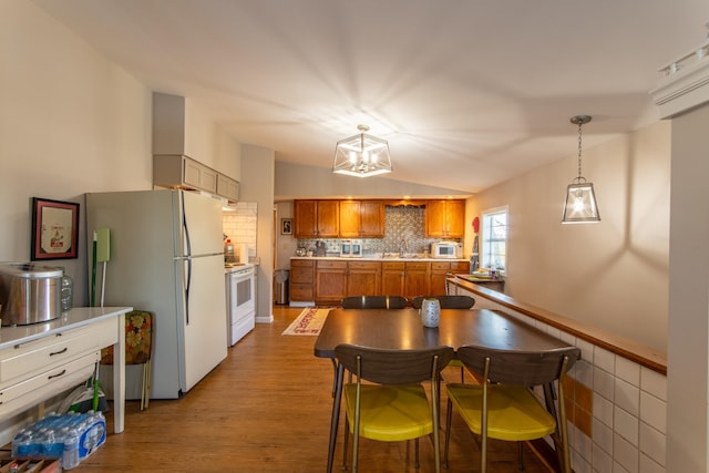 kitchen with pendant lighting, white appliances, an inviting chandelier, light wood-type flooring, and vaulted ceiling