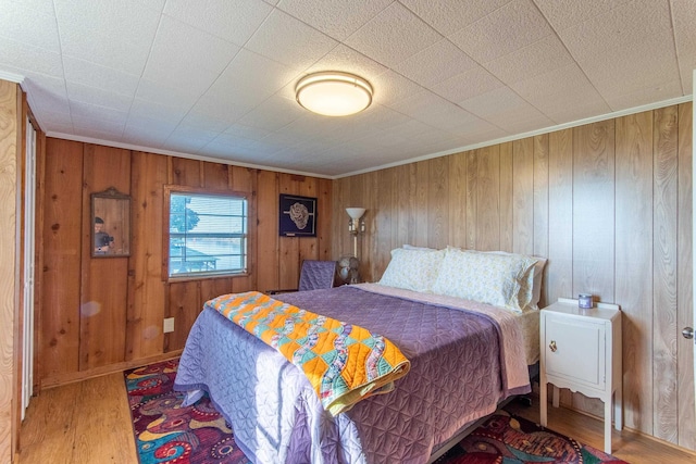 bedroom with wood walls, wood finished floors, and ornamental molding