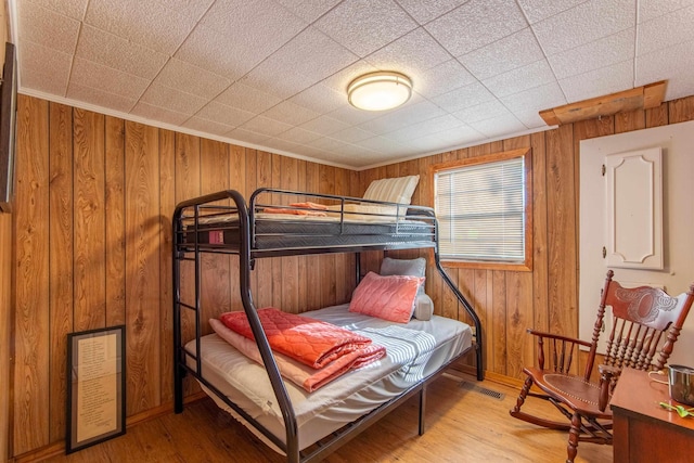 bedroom featuring wooden walls, wood finished floors, visible vents, and baseboards