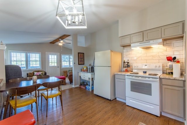 kitchen with vaulted ceiling, light wood-style floors, decorative backsplash, white appliances, and under cabinet range hood