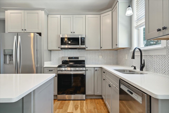 kitchen featuring appliances with stainless steel finishes, tasteful backsplash, light wood-type flooring, decorative light fixtures, and sink