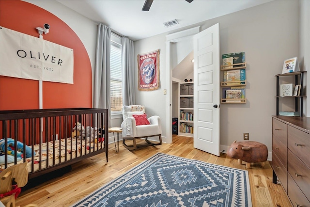 bedroom featuring a crib, light hardwood / wood-style flooring, and ceiling fan