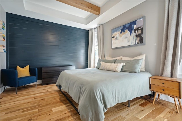 bedroom featuring light wood finished floors, wooden walls, beam ceiling, and an accent wall