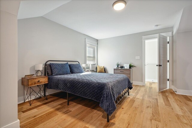 bedroom with light wood finished floors, baseboards, and vaulted ceiling