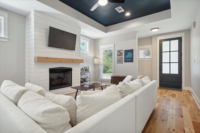 living area featuring hardwood / wood-style floors, a large fireplace, a raised ceiling, visible vents, and a ceiling fan