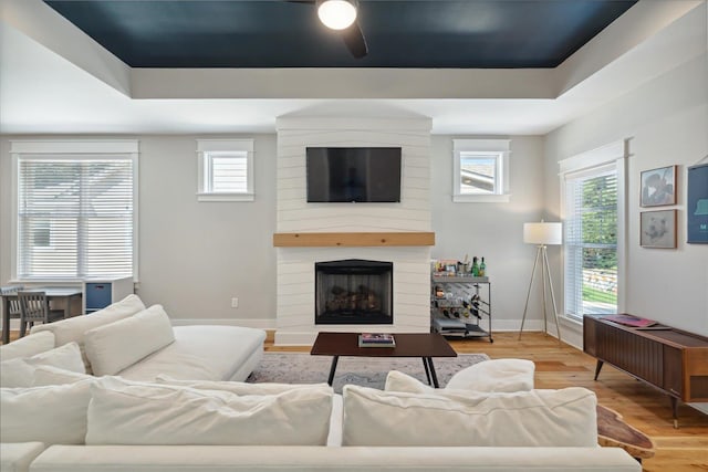 living room with a large fireplace, ceiling fan, a raised ceiling, and hardwood / wood-style floors