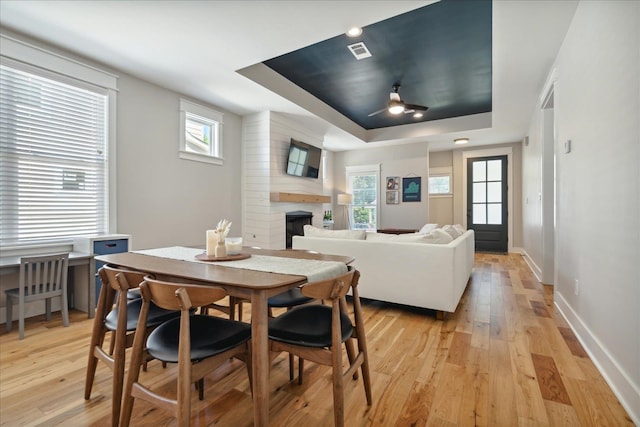 dining space featuring a healthy amount of sunlight, a tray ceiling, light hardwood / wood-style flooring, and a fireplace