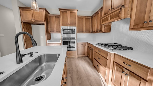 kitchen featuring sink, light wood-type flooring, tasteful backsplash, decorative light fixtures, and stainless steel appliances