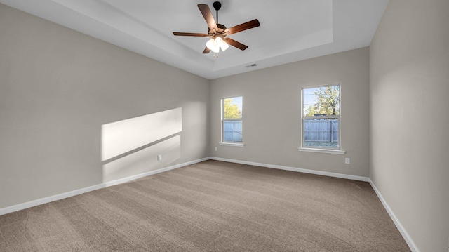 carpeted spare room with a tray ceiling and ceiling fan