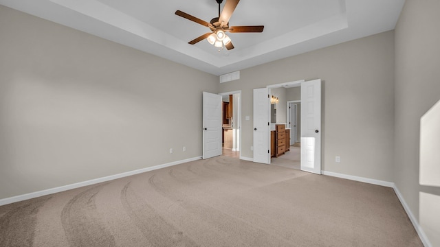 unfurnished bedroom with a tray ceiling, connected bathroom, ceiling fan, and light carpet