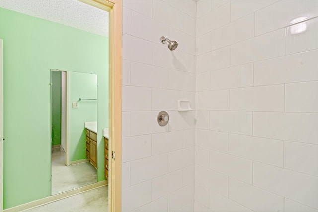 bathroom with a textured ceiling, vanity, and tiled shower