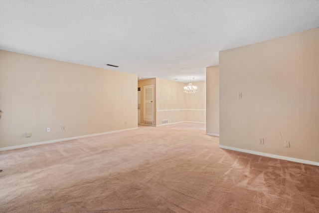 empty room with a notable chandelier, a textured ceiling, and carpet floors