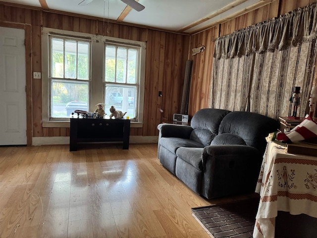 living room featuring ceiling fan, light wood-type flooring, and wood walls