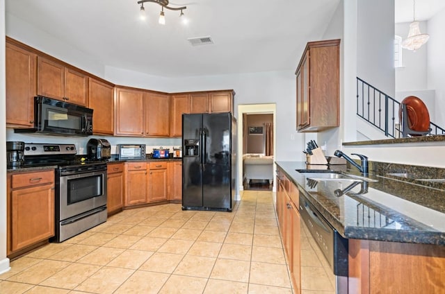 kitchen featuring dark stone counters, light tile patterned flooring, sink, hanging light fixtures, and black appliances