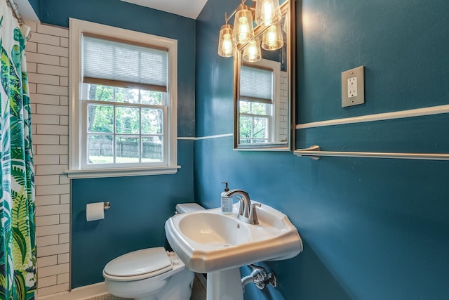 bathroom with a shower with shower curtain, sink, toilet, and a healthy amount of sunlight