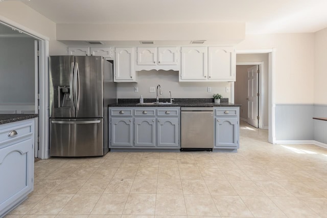 kitchen with sink, white cabinetry, gray cabinets, stainless steel appliances, and dark stone counters