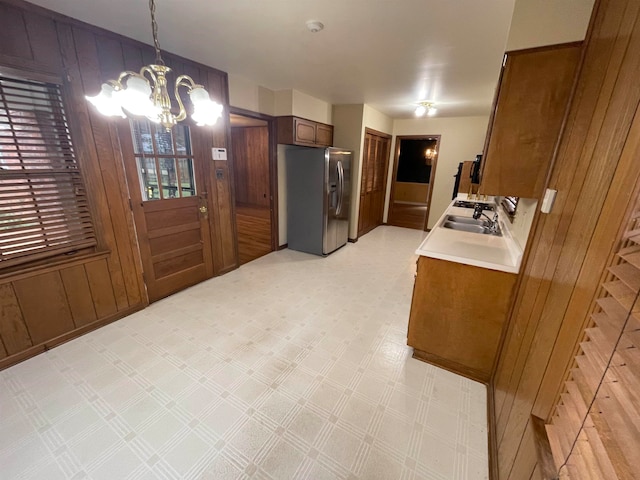 kitchen with pendant lighting, wood walls, sink, stainless steel refrigerator with ice dispenser, and a notable chandelier