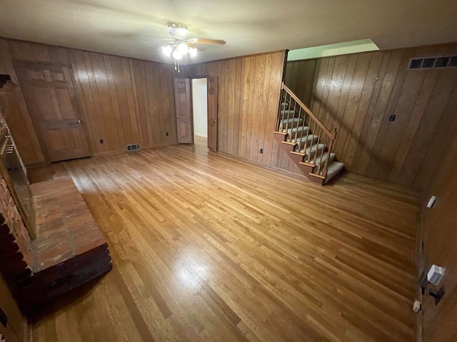 unfurnished living room featuring wooden walls, ceiling fan, and hardwood / wood-style flooring