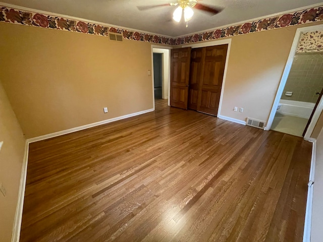 unfurnished bedroom featuring wood-type flooring, ensuite bath, ceiling fan, and a closet