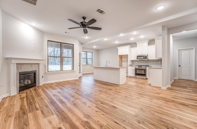 unfurnished living room with sink, a fireplace, ceiling fan, and light hardwood / wood-style flooring