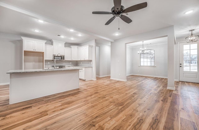 kitchen with light hardwood / wood-style flooring, an island with sink, light stone countertops, decorative backsplash, and white cabinets