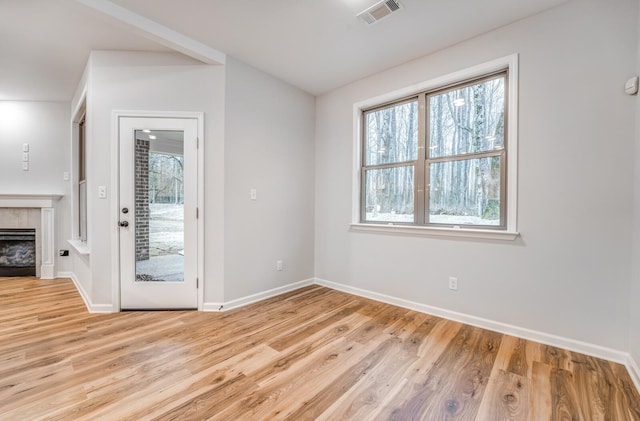 spare room featuring vaulted ceiling, a tile fireplace, and light wood-type flooring