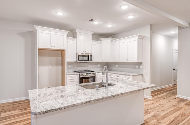 kitchen featuring appliances with stainless steel finishes, white cabinetry, sink, light stone countertops, and a center island with sink