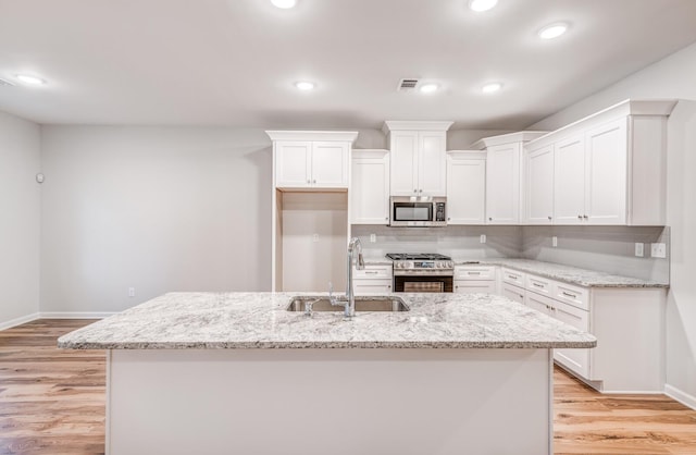 kitchen with sink, light stone counters, an island with sink, stainless steel appliances, and white cabinets