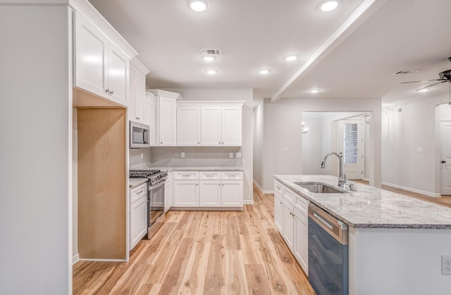 kitchen featuring white cabinetry, sink, stainless steel appliances, a center island with sink, and light hardwood / wood-style flooring