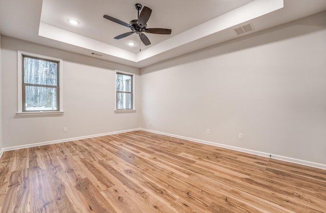 empty room with a tray ceiling, light hardwood / wood-style floors, and ceiling fan