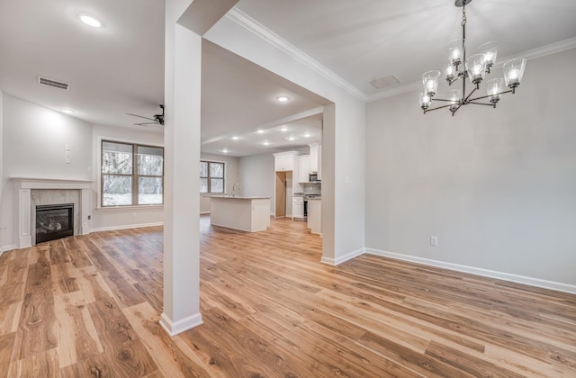 unfurnished living room with ceiling fan with notable chandelier, light hardwood / wood-style flooring, and ornamental molding